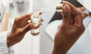 Dłonie trzymają buteleczkę z serum. Pipeta z kroplą produktu, być może zawierającego kwas ferulowy, jest gotowa do aplikacji.