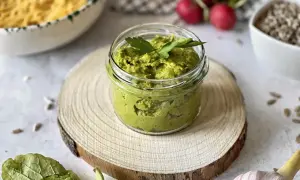 Domowe, tradycyjne pesto przepis. Zielona pasta w słoiczku, obok czosnek, rzodkiewki i nasiona słonecznika.