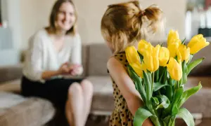 Mała dziewczynka z bukietem żółtych tulipanów za plecami, przygotowuje życzenia urodzinowe dla cioci.