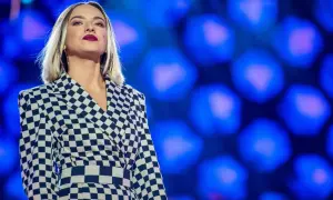 Młoda, amerykańska piosenkarka country w stylowej, szachownicowej marynarce na tle niebieskich świateł.