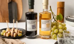 Zwei Flaschen Balsamico und Condimento Bianco, daneben Käsewürfel mit Balsamico und Trauben.