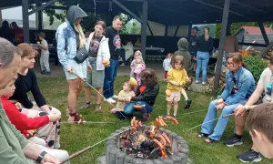 Rodzina piecze kiełbaski nad ogniskiem, czuć puls miasta w tej sielskiej atmosferze.