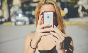 Kobieta trzyma iPhone'a przed twarzą, zasłaniając ją.