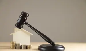 Młotek sędziowski nad domkiem i monetami symbolizuje zawieszenie postępowania egzekucyjnego.