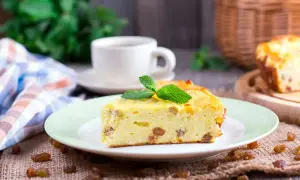 Una fetta di torta putana, soffice e dorata, con uvetta e una fogliolina di menta, accanto a una tazza di caffè.