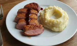 Soczysta pierś z kaczki, pokrojona w plastry, polana sosem, obok porcja purée ziemniaczanego.