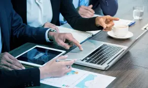 Persone in abiti eleganti collaborano a un tavolo, analizzando dati su tablet e laptop. Sono le risorse umane che lavorano insieme per il successo.