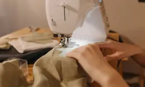 Ręce prowadzą materiał pod maszynę do szycia, by nauczyć się, jak zwęzić sukienkę w ramionach.
