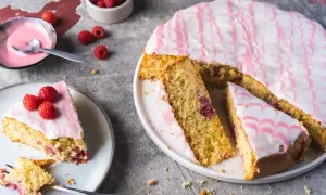 Ein himbeerkuchen, einfach aber extrem lecker, mit rosa Zuckerguss und frischen Himbeeren. Ein Stück ist bereits angeschnitten.