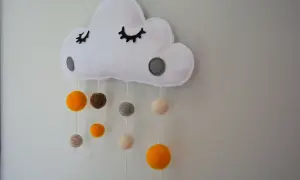 Urocza girlanda chmurki z filcu, ozdobiona kropkami i zwisającymi pomponami w kolorach ziemi. Idealna do pokoju dziecięcego.