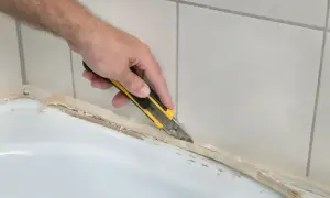Dłoń z nożem odcina stary silikon przy wannie. Poznaj, jak usunąć stary silikon krok po kroku.