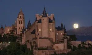 El majestuoso castillo de Segovia se alza bajo una luna llena, con su imponente arquitectura y torres que parecen vigilar la noche.