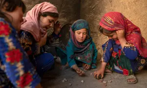 Vier Mädchen spielen mit Steinen. Ihre Kleidung und Kopftücher spiegeln die afghanische Kultur wider.