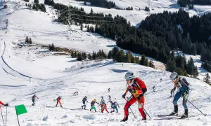 Skibergsteigen-Athleten kämpfen sich einen verschneiten Hang hinauf, bereit für olympische Herausforderungen.