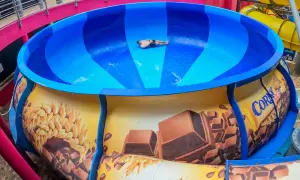 Mann rutscht in einer riesigen blauen Schüssel einer Wasserrutsche, die mit Schokolade und Getreide dekoriert ist. Ein Spaß im Prag!