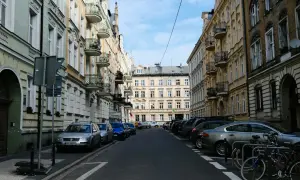 Ulica w kamienicach, typowa dla **południa Polski**. Samochody stoją zaparkowane wzdłuż chodnika, a na pierwszym planie widać rowery.