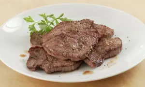 Saftiges Schnitzel Natur, gewürzt mit Pfeffer und Salz, auf einem weißen Teller mit Petersilie garniert.