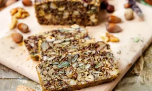 Slices of hearty keto brot, packed with seeds and nuts, rest on a wooden board.
