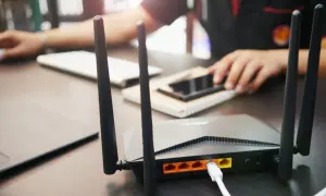 Router co to? Urządzenie z antenkami, podłączone kablem, zapewniające łączność internetową. W tle osoba korzystająca z komputera.
