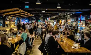 Tętniący życiem food hall Metropolia, gdzie ludzie jedzą i piją przy długich stołach, a w tle widać bary i stoiska z jedzeniem.