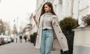 Styling Mom Jeans: Ein lässiger Look mit Strickpullover, Trenchcoat und Perlenschmuck auf der Straße.