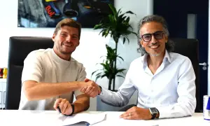 Max Verstappen sonríe mientras estrecha la mano de un hombre con gafas, sellando un acuerdo.