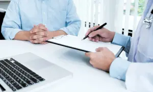 Lekarz pisze na kartce, pacjent siedzi naprzeciwko.