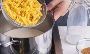 Eine Hand schüttet Spiralnudeln in einen Topf mit Milch. Zutaten für milch nudeln.