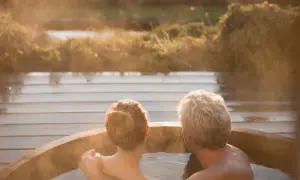 Pareja disfrutando de una relajante experiencia en un jacuzzi al atardecer. El vapor se eleva mientras se abrazan, creando un momento íntimo.