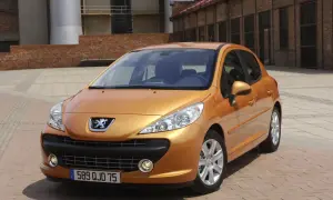 Pomarańczowy Peugeot 207 1.4 benzyna zaparkowany na placu z ceglaną posadzką, w tle budynki przemysłowe.