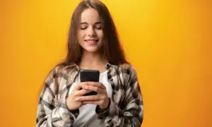 Uśmiechnięta dziewczyna z telefonem w dłoniach, szuka informacji, jak sprawdzić stan konta w Orange na kartę.