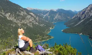 Frau genießt Ausblick beim Plansee Wandern. Türkiser See, grüne Berge und blauer Himmel.