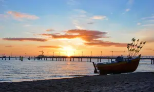 Łódź rybacka na plaży o zachodzie słońca, w tle molo i morze.