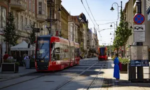 Czerwony tramwaj na ulicy w Katowicach. W tle kamienice i inny tramwaj. To widok na katowice stare miasto.