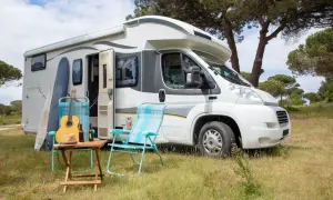 En vit husbil, en personbil klass 2, står parkerad i gräset. Surfbrädor, en gitarr och campingstolar antyder en avkopplande semester.
