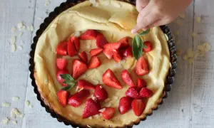 Puszysty dutch baby z truskawkami i płatkami migdałów, dekorowany przez dziecko.