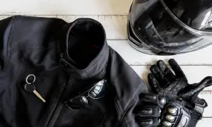 Czarna kurtka motocyklowa, kask, rękawice, okulary i kluczyk na białym tle.