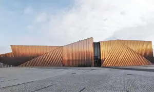 Nowoczesny budynek muzeum ognia z miedzianą elewacją, przypominającą płomienie.