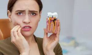 Kobieta z bólem zęba trzyma model z widoczną czarną kropką na plombie, wskazującą na próchnicę.