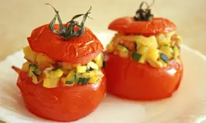 Deux tomates farcies, garnies d'un mélange de légumes et de fromage, sont présentées sur une assiette blanche.