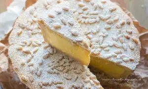 Una fetta di torta della nonna, cosparsa di pinoli e zucchero a velo, mostra il suo ripieno cremoso.