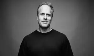 Porträtt av Magnus Lindqvist, en man med gråsprängt hår och ett vänligt leende, klädd i en svart t-shirt.