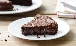Una fetta di torta al cioccolato senza farina e burro, densa e umida, su un piatto bianco.