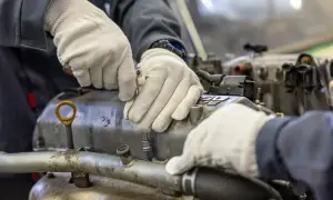 Mechanik w białych rękawiczkach sprawdza, jak sprawdzić drożność kanałów olejowych w bloku silnika, używając klucza nasadowego.