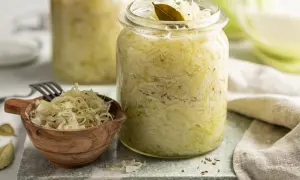 Frisches Sauerkraut im Glas, bereit für ein leckeres Sauerkraut Rezept. Ein kleiner Holzlöffel mit Sauerkraut und Lorbeerblätter liegen daneben.