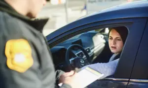 Policjant wręcza kobiecie w samochodzie dokumenty. Wygląda na to, że chodzi o mandaty w Austrii.