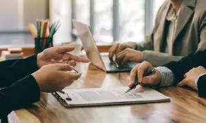 Ludzie przy biurku omawiają dokumenty, jeden pisze na laptopie.