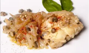 Un morceau de lotte poisson, cuisiné avec des oignons, des câpres et des épices, garni de feuilles de basilic.
