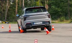 Szary SUV wykonuje test łosia, gwałtownie skręcając między pomarańczowymi pachołkami na torze.
