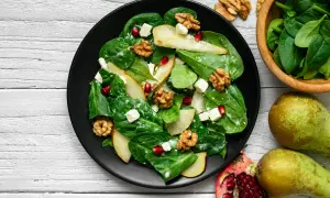 Sałatka z granatem, gruszką, orzechami i serem feta na talerzu. Pyszne połączenie smaków i kolorów.